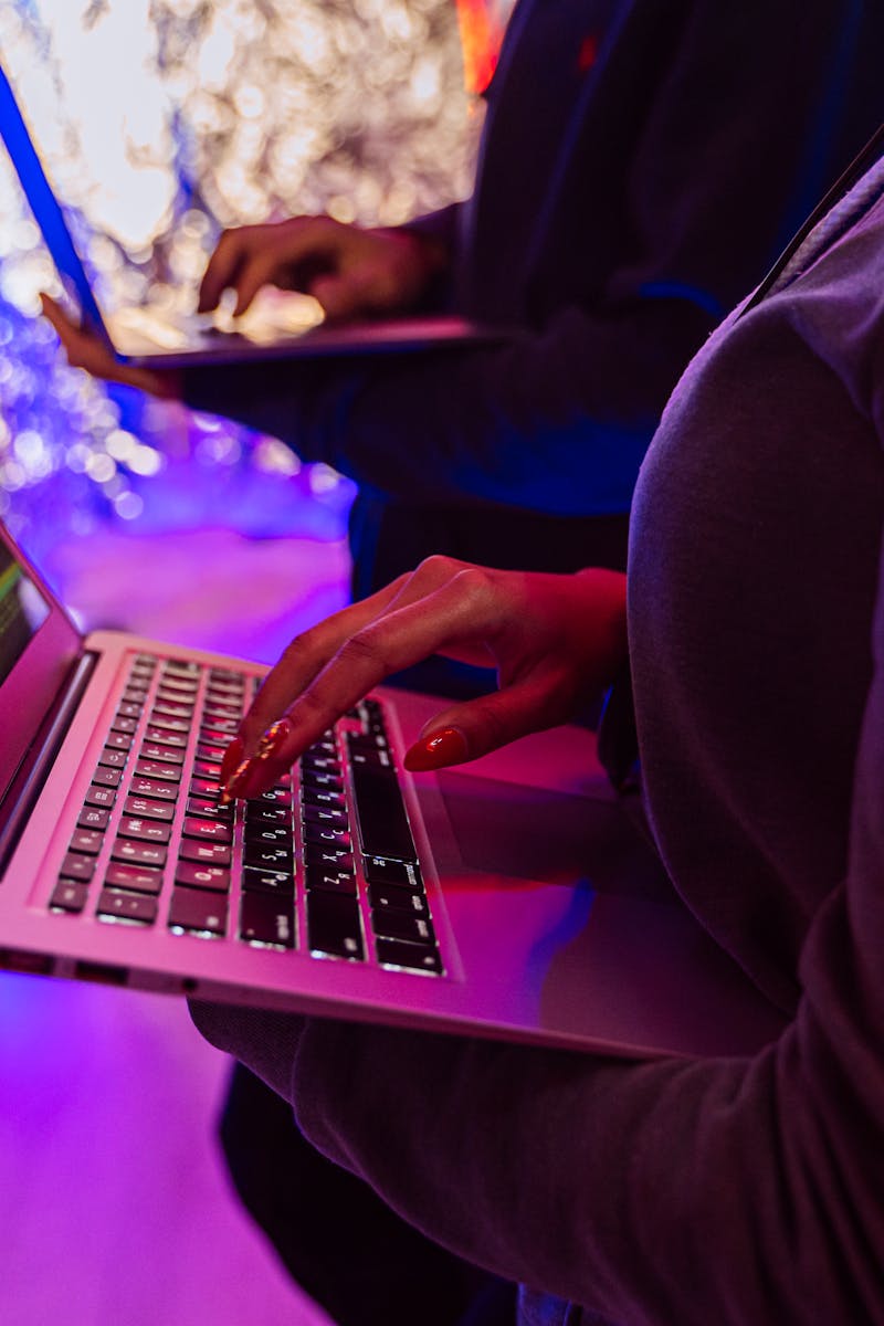 Two professionals analyzing data on laptops with colorful lighting, focusing on cybersecurity details.
